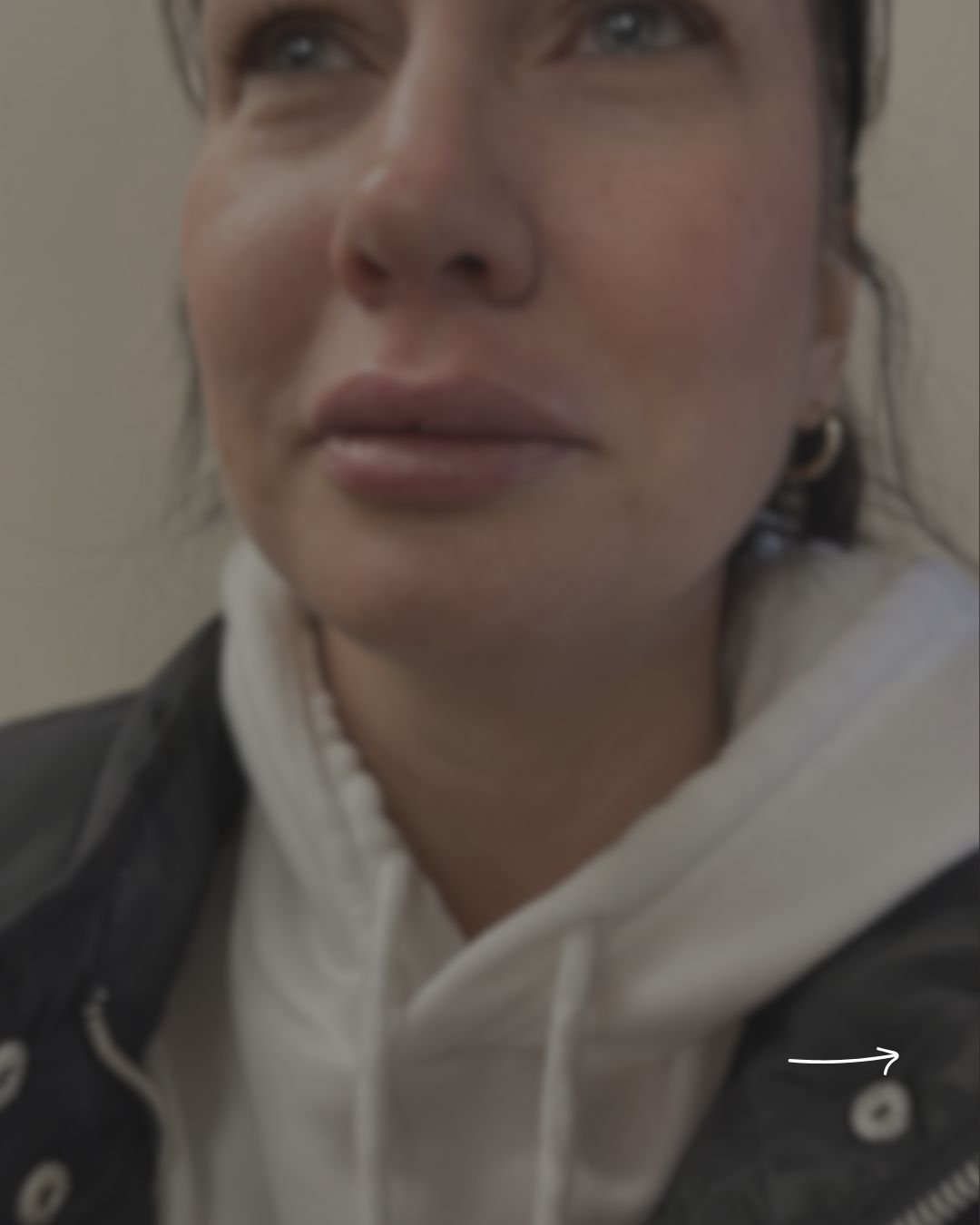 Close-up of a person wearing a white hooded sweatshirt under a dark jacket, with a small white arrow overlay near the lower right side.