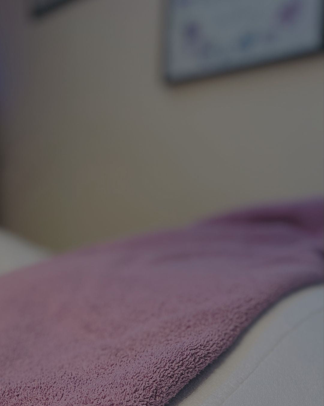 A close-up of a soft, textured mauve-purple towel draped over a white surface in a softly blurred indoor setting.